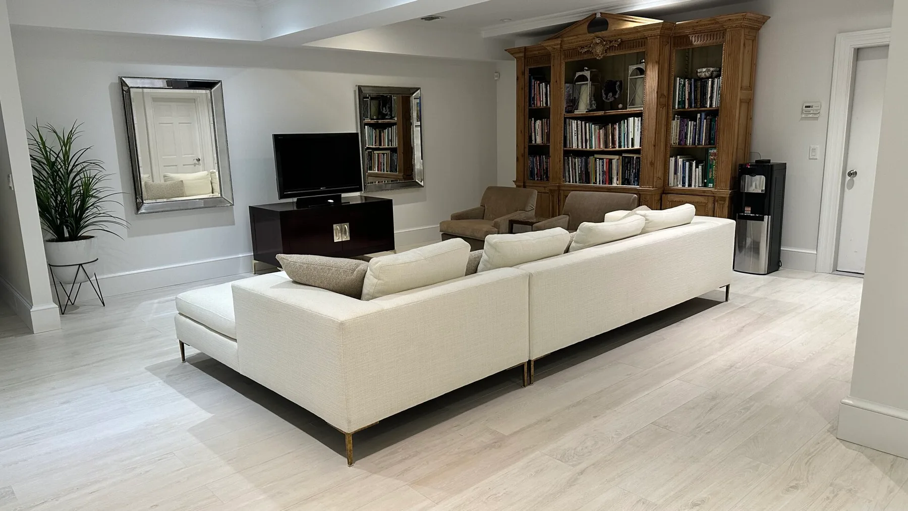 A living room with white seating, a television, and a large bookcase.