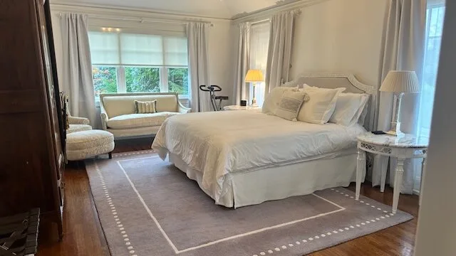 A bright bedroom with a large bed and a sitting area by the windows.