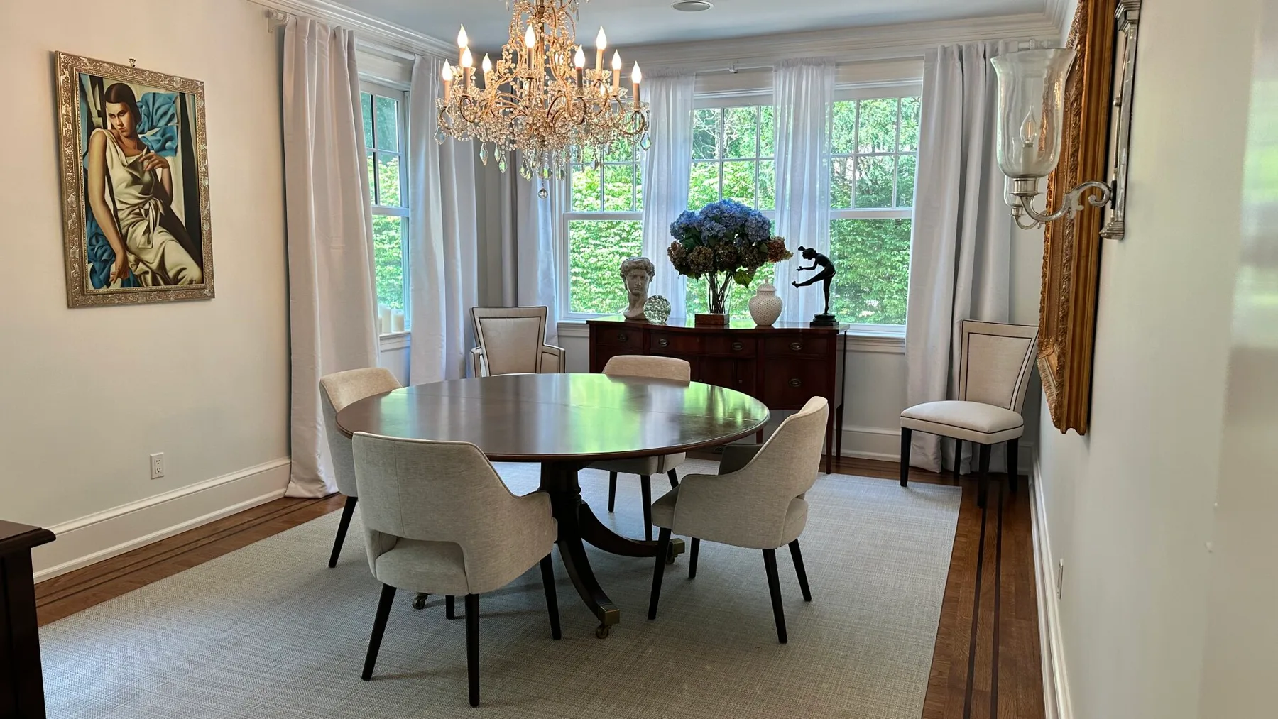 A dining room with a round table and upholstered seating beside large windows.