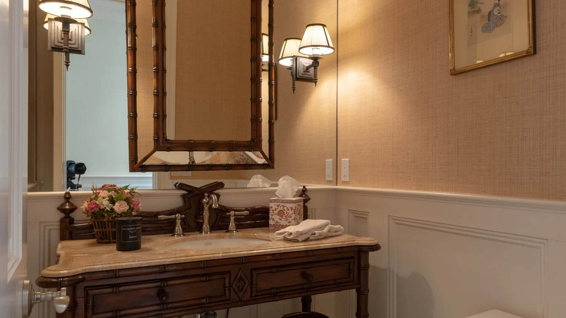 A bathroom vanity with a large mirror, wall sconces, and a flower arrangement.