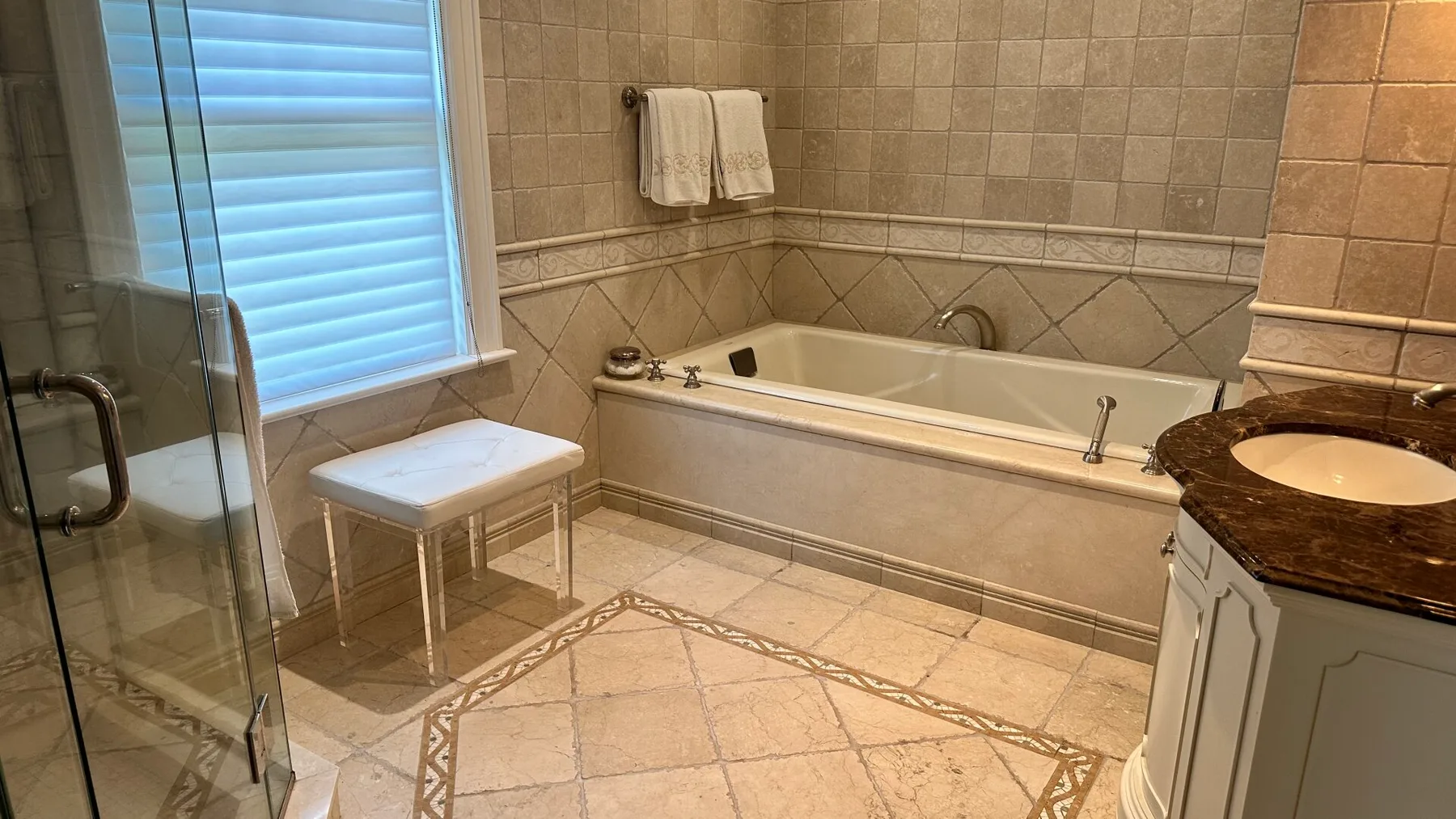 A tiled bathroom with a bathtub and glass shower beside a window.