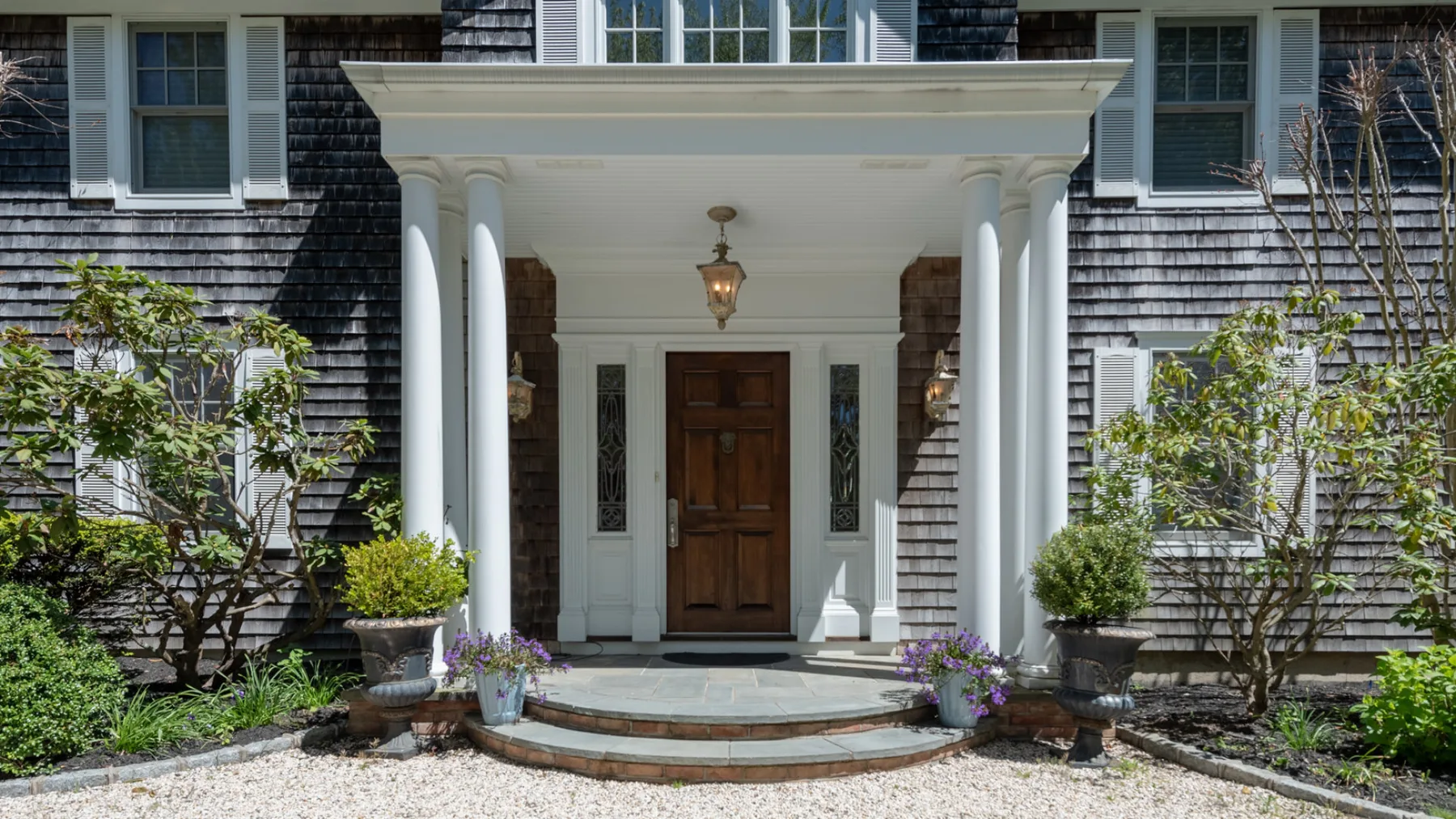 A covered front entrance with a wooden door, white columns, and potted flowers.