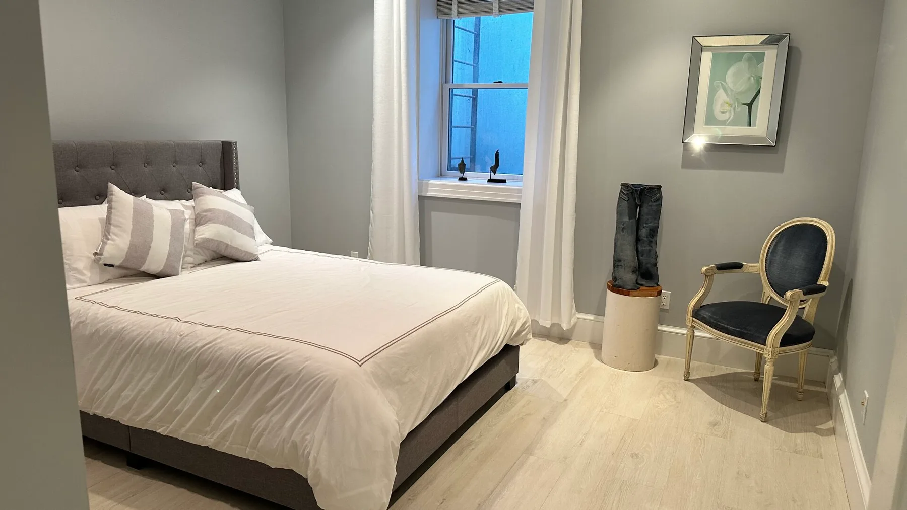 A bedroom with a neatly made bed, a window, and a chair.