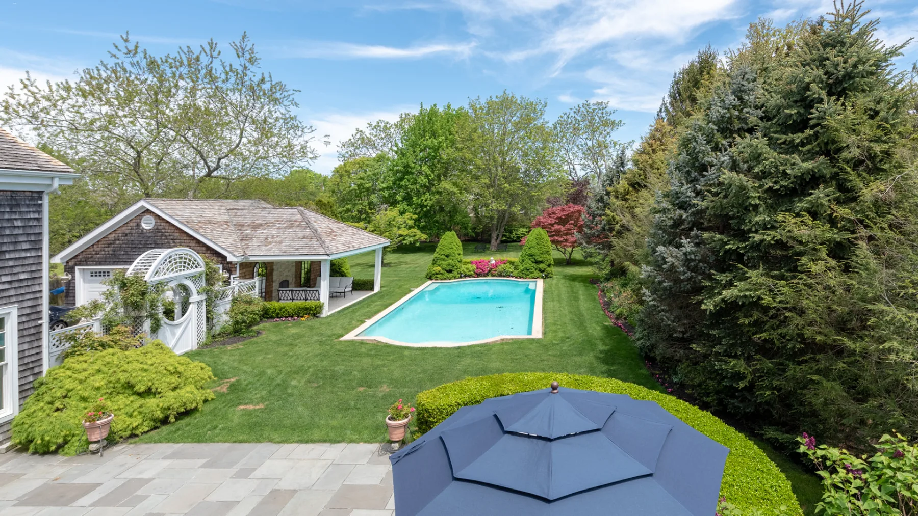 An outdoor swimming pool sits beside a landscaped lawn and patio.