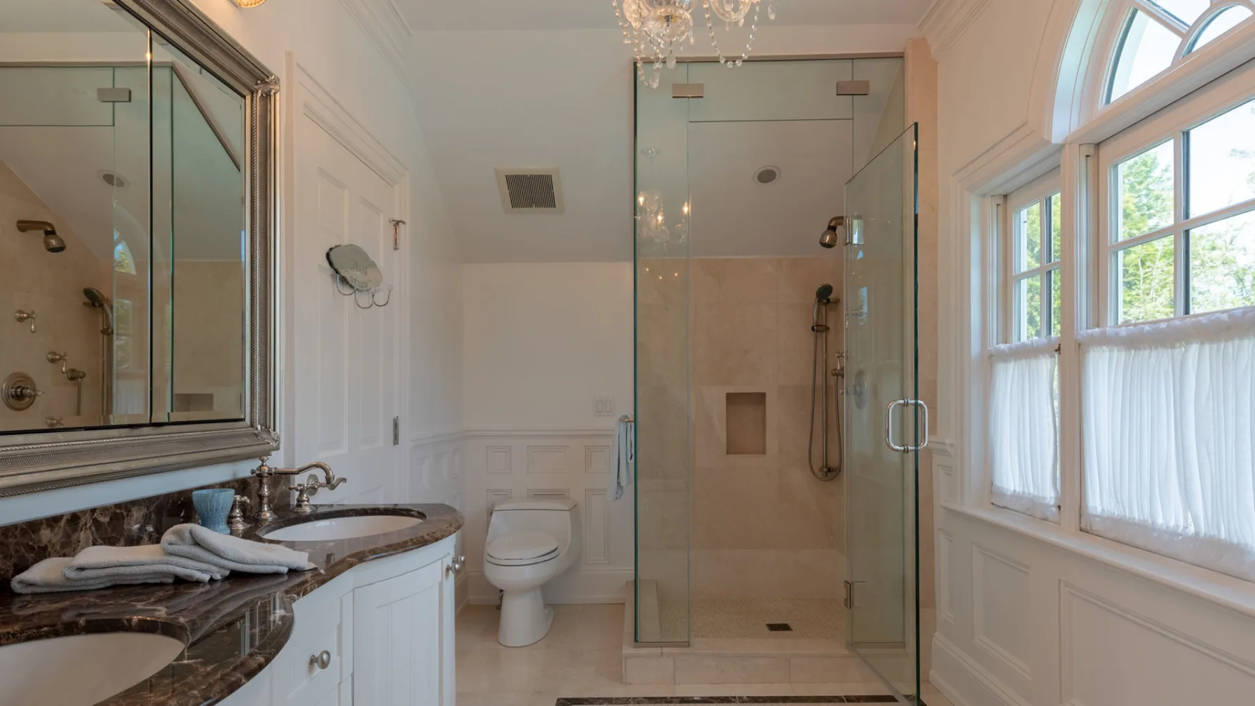 A bright bathroom with a glass shower, vanity, and windows.