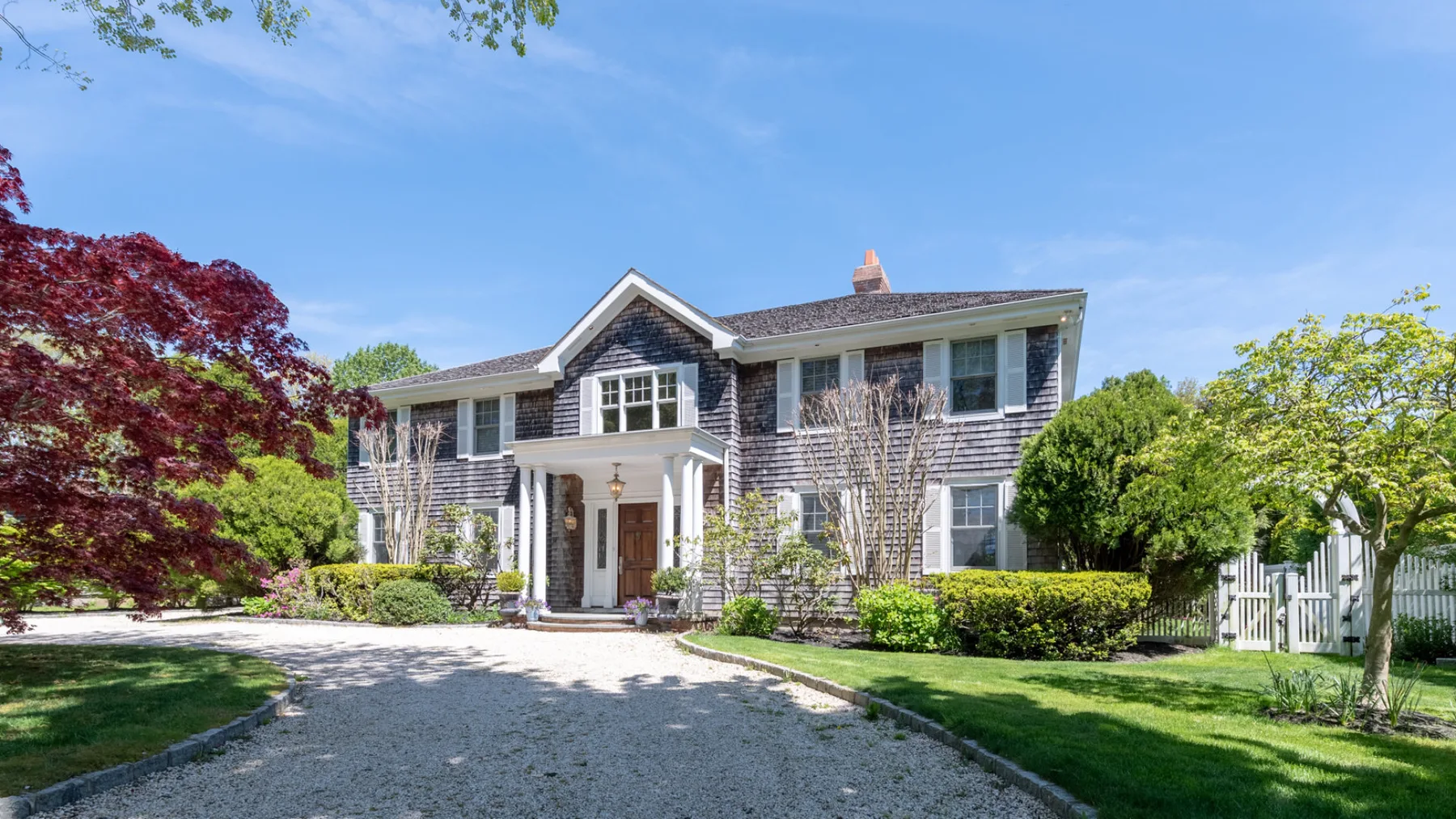 A large two-story house stands at the end of a curved gravel driveway.