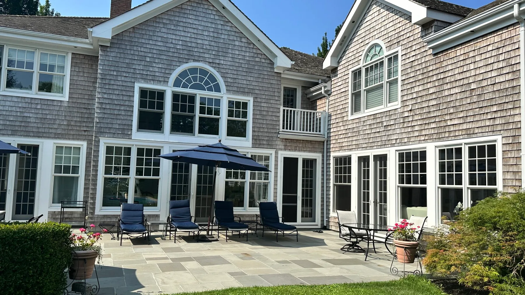 A paved outdoor patio with seating and a large house in the background.
