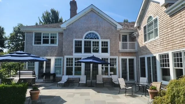 A paved patio with outdoor seating and umbrellas in front of a large house.