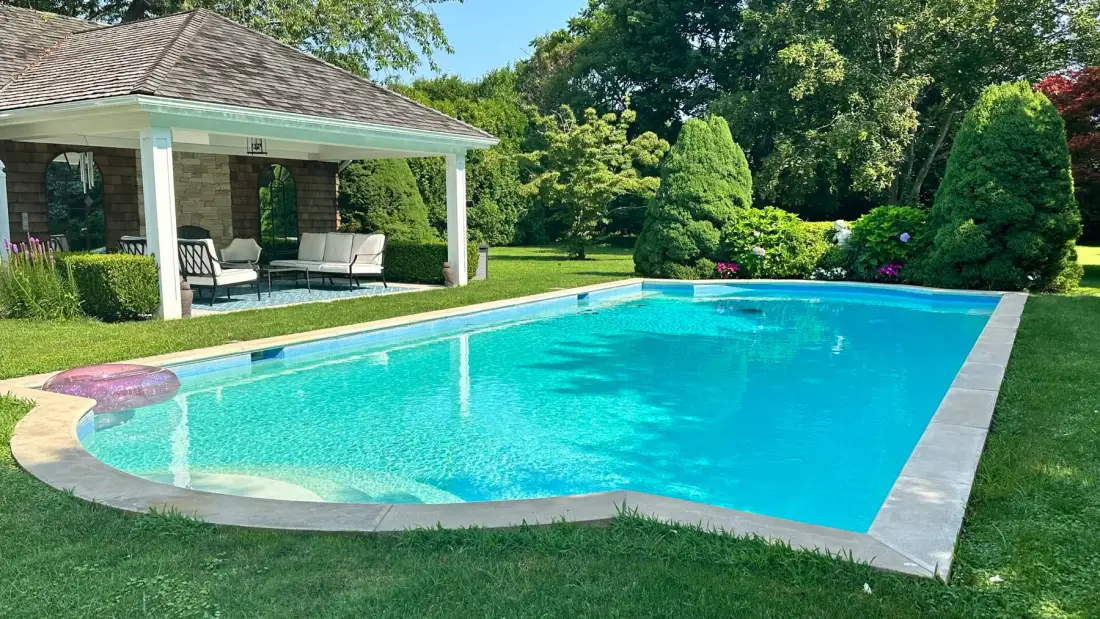 A swimming pool beside a covered seating area in a landscaped garden.