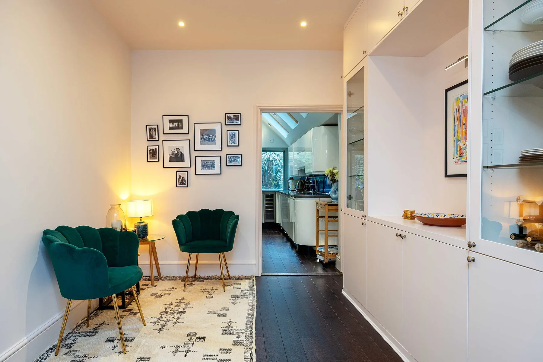 A sitting area with green seating and framed pictures beside a kitchen.