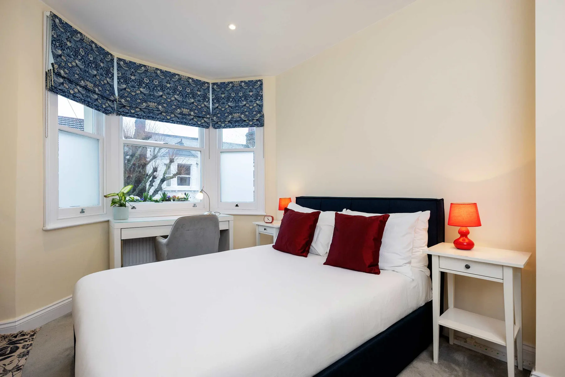 A bedroom with a bed beneath windows dressed with patterned blue blinds.