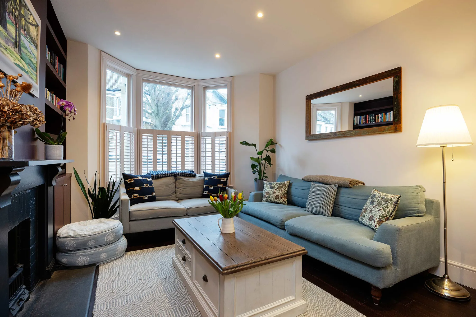 A bright living room with blue seating, a wooden coffee table, and bay windows.