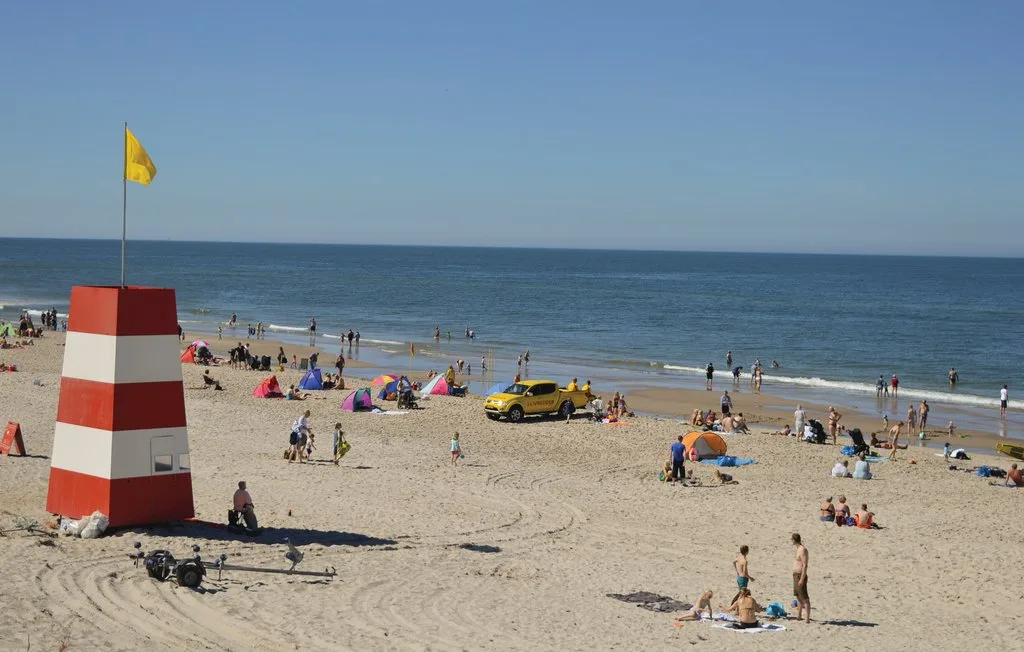 Una playa de arena concurrida, con bañistas y sombrillas de colores junto a la orilla.
