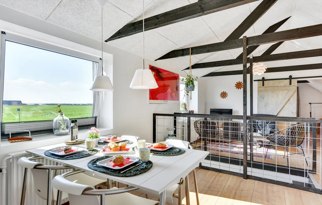 Un comedor con la mesa puesta está junto a una ventana grande con vistas a un paisaje verde.