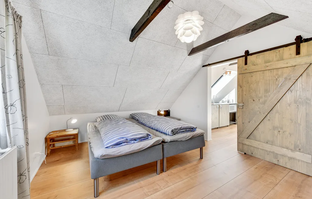 Un dormitorio con dos camas bajo un techo inclinado y una puerta de madera abierta.