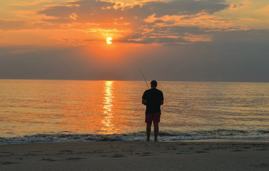 Una persona está en la playa al atardecer, mirando hacia el agua.