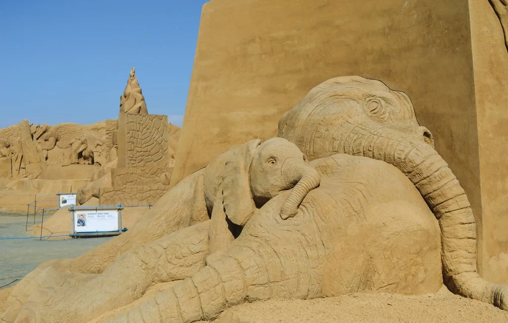 Una gran escultura de arena representa a un elefante adulto con una cría apoyada contra él.
