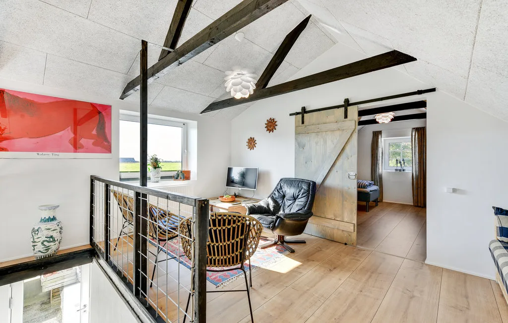 Una luminosa sala tipo loft tiene vigas oscuras expuestas y una barandilla junto a la escalera.