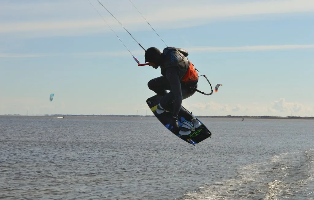 Una persona practica kitesurf y salta sobre el agua mientras sujeta las líneas de la cometa.