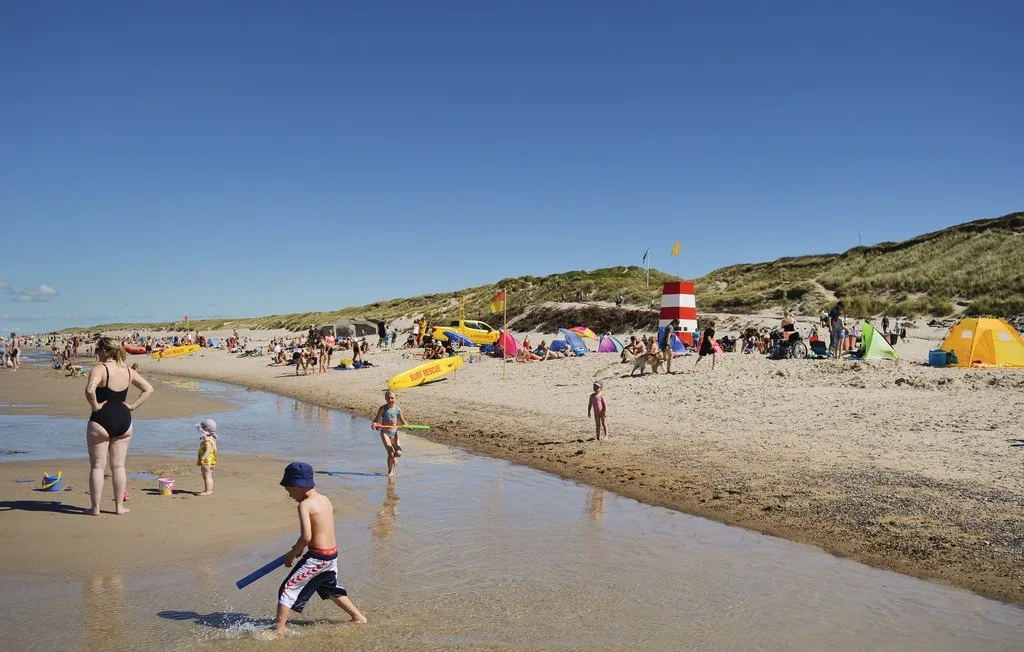 Una playa concurrida con personas caminando por aguas poco profundas y tomando el sol en la arena.