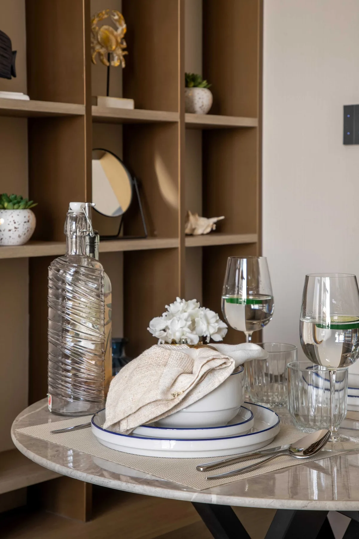 A set dining table stands in front of a tall brown shelving unit.