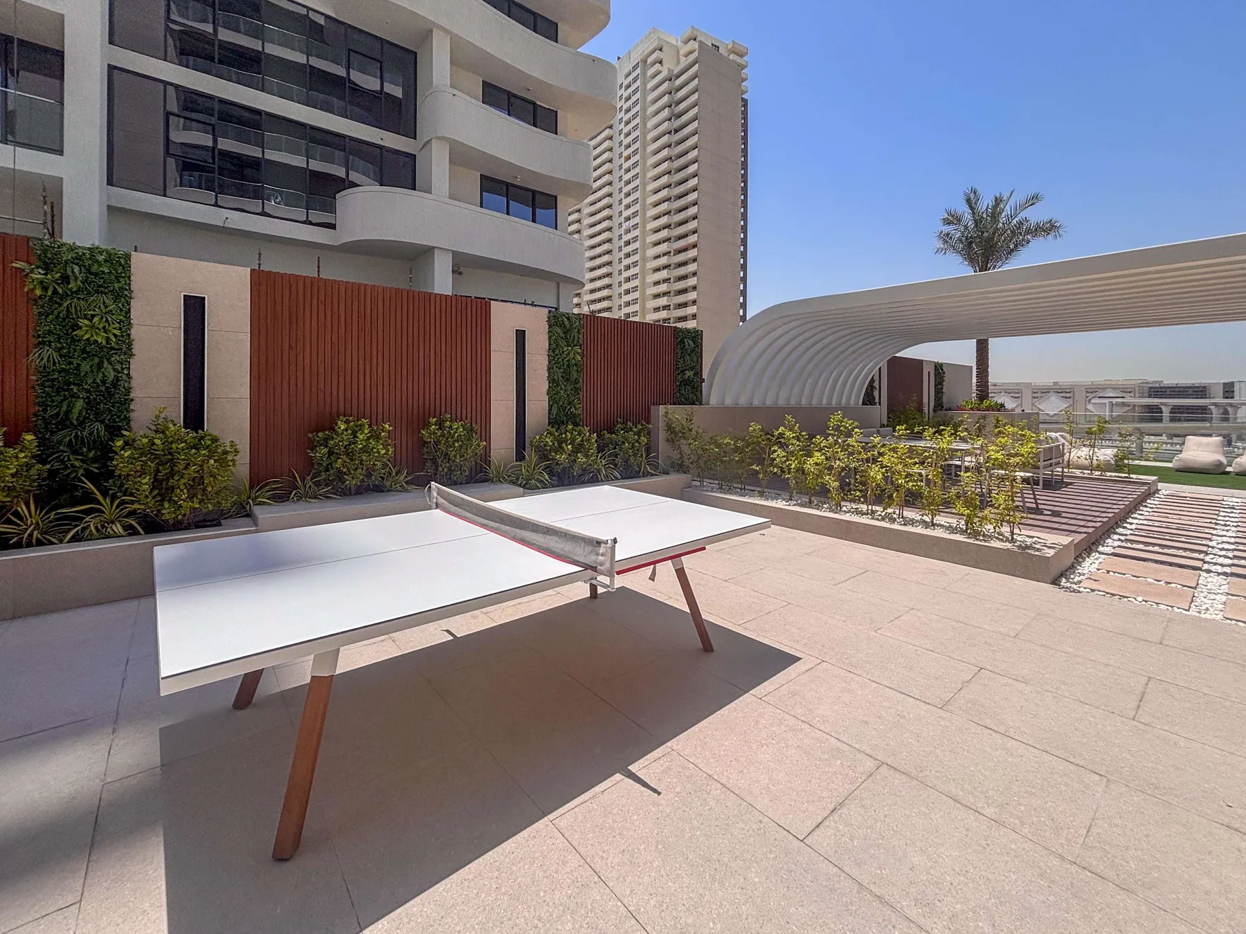 A rooftop recreation area with a table tennis table beside landscaped planters.