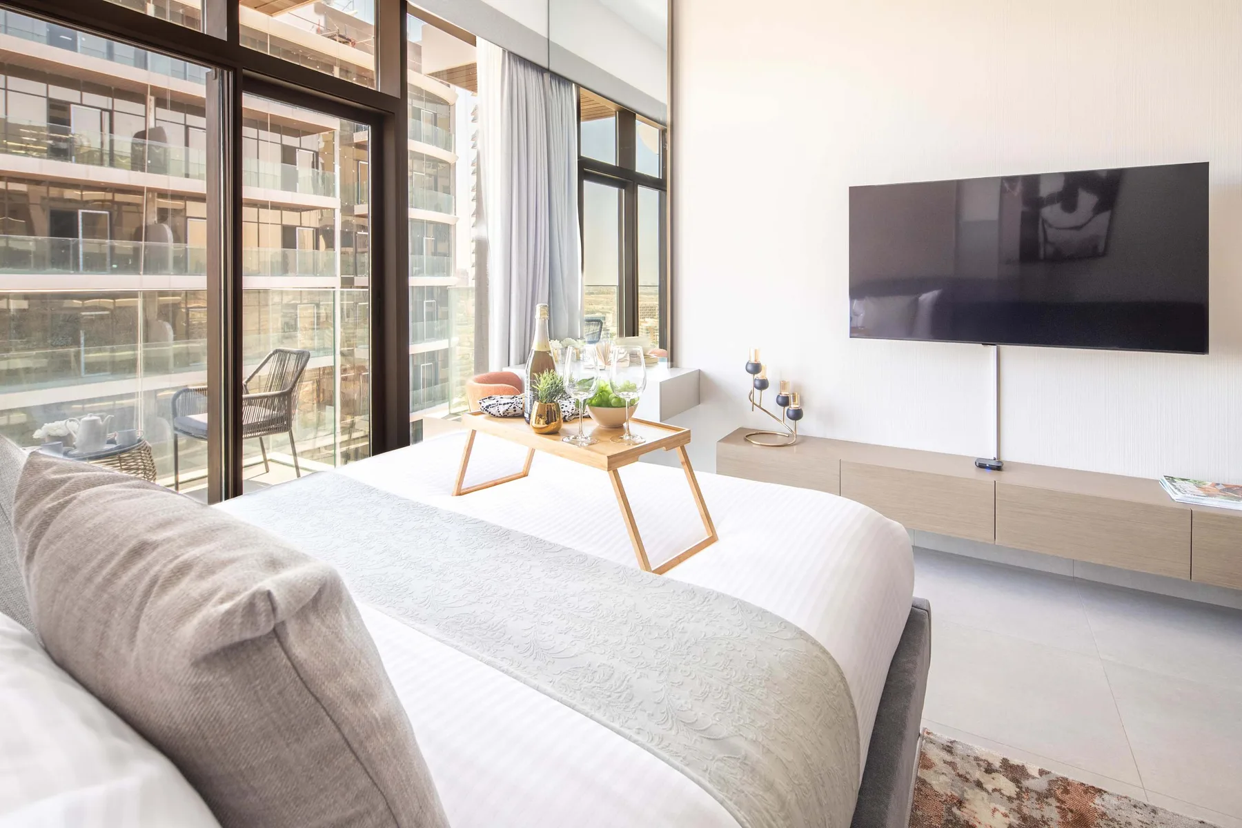 A bright bedroom with a bed beside large windows and a wall-mounted television.