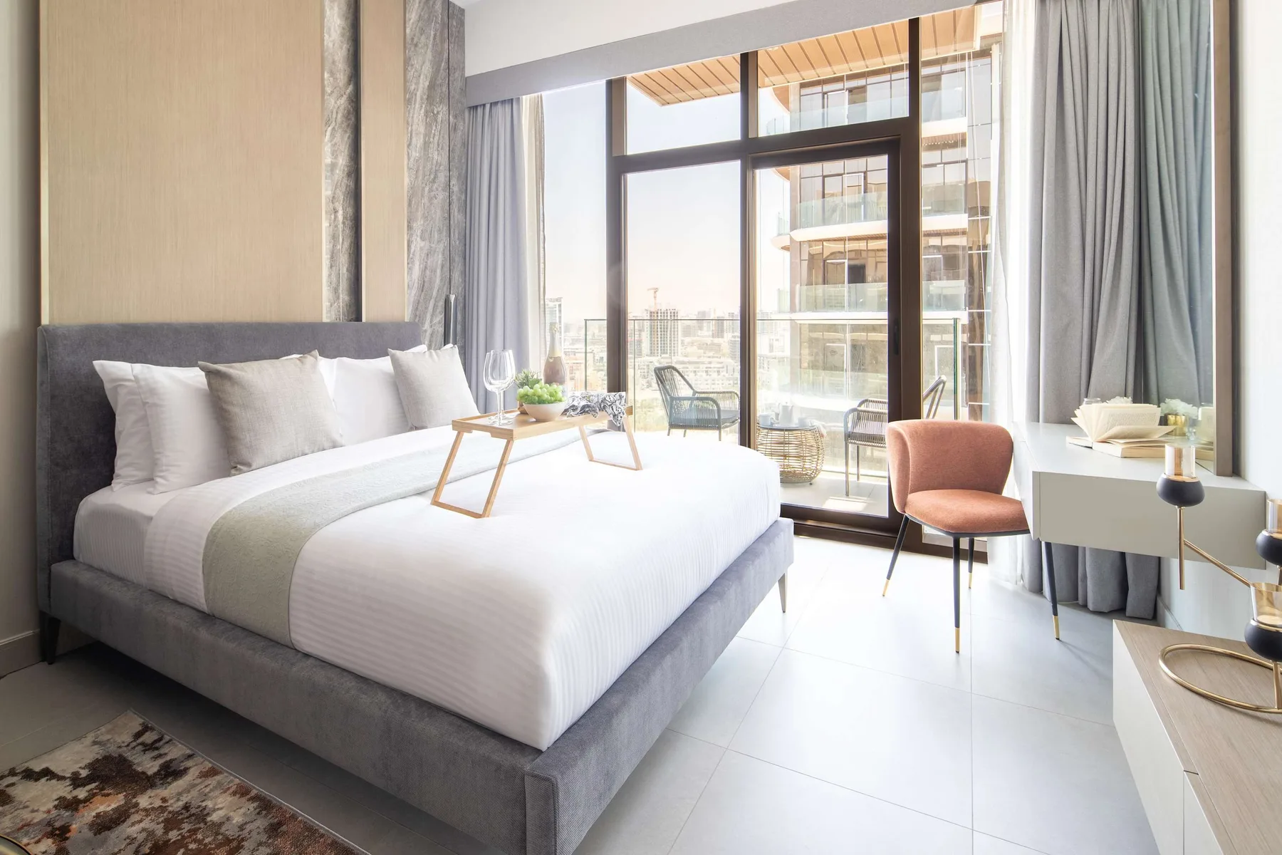 A bright bedroom with a neatly made bed beside floor-to-ceiling windows.