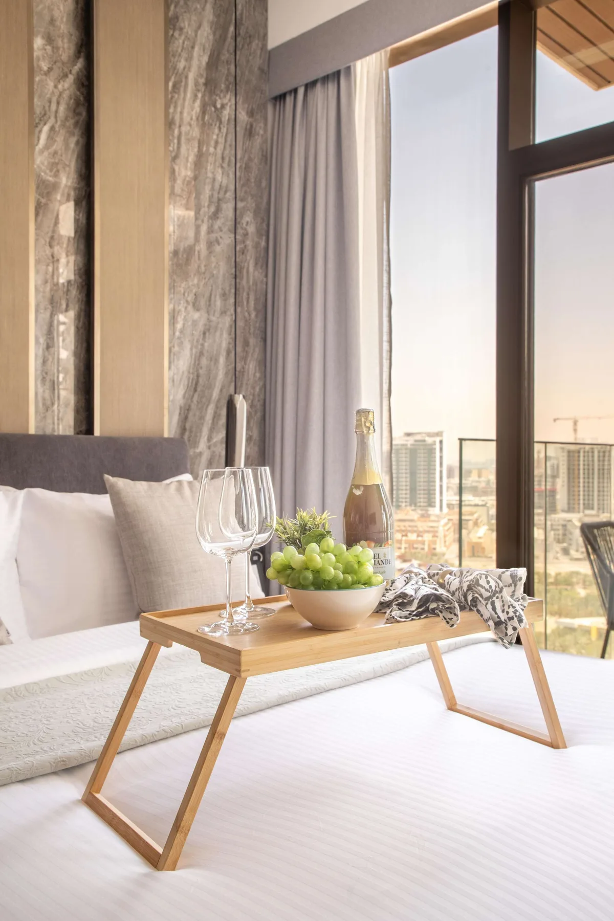 A bedroom with a low table holding fruit and glasses beside a large window.