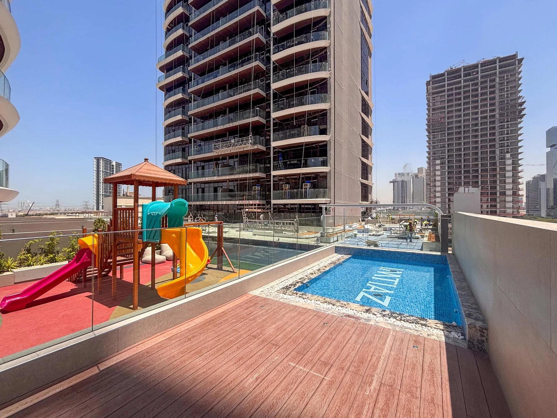 A rooftop pool and children’s play area sit beside tall residential buildings.