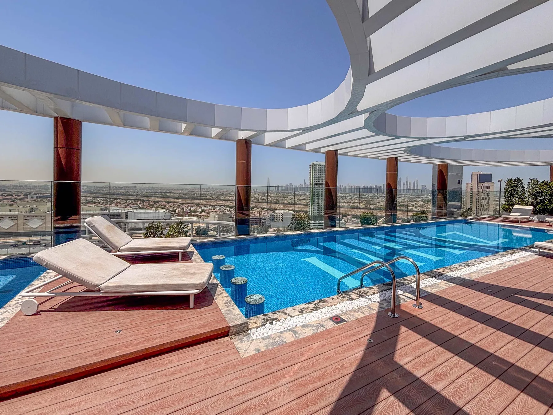 A rooftop swimming pool beneath a curved canopy, with loungers along the deck.