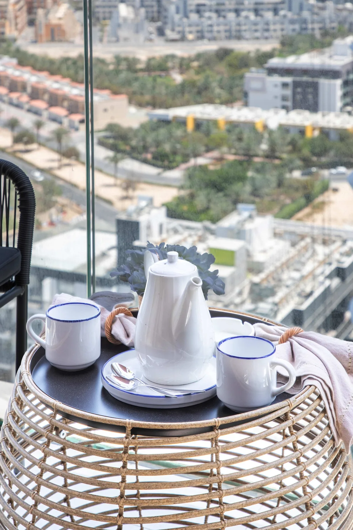 A tea service sits on a round table beside a window overlooking the city.