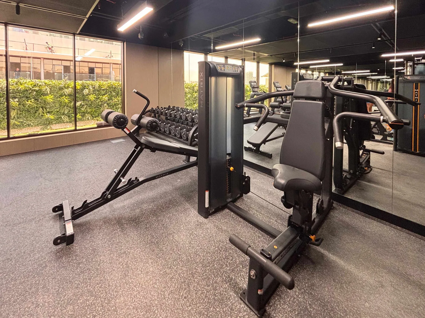A gym with weight machines and exercise equipment beside large windows.