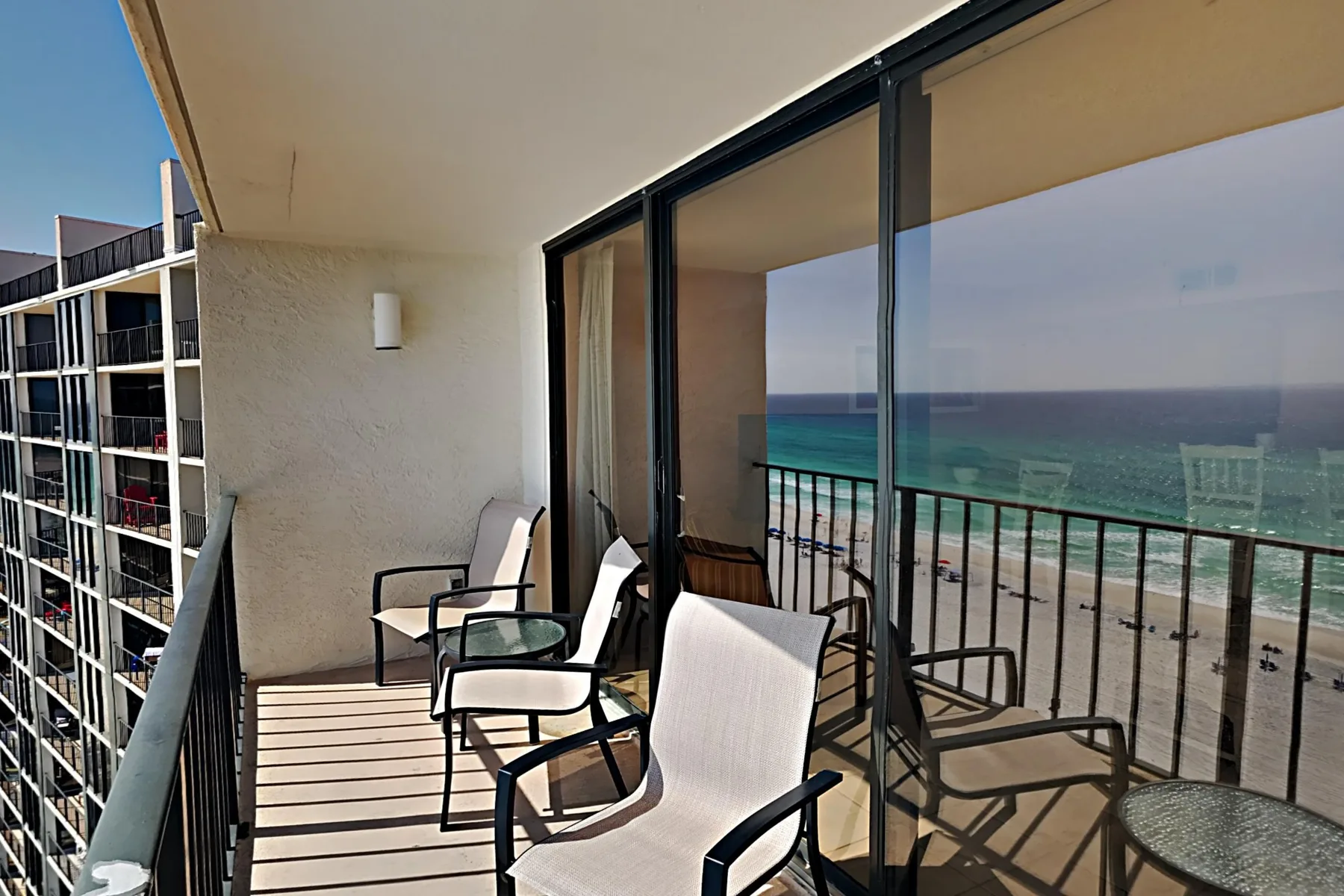 A balcony with seating overlooks the ocean through a glass door.
