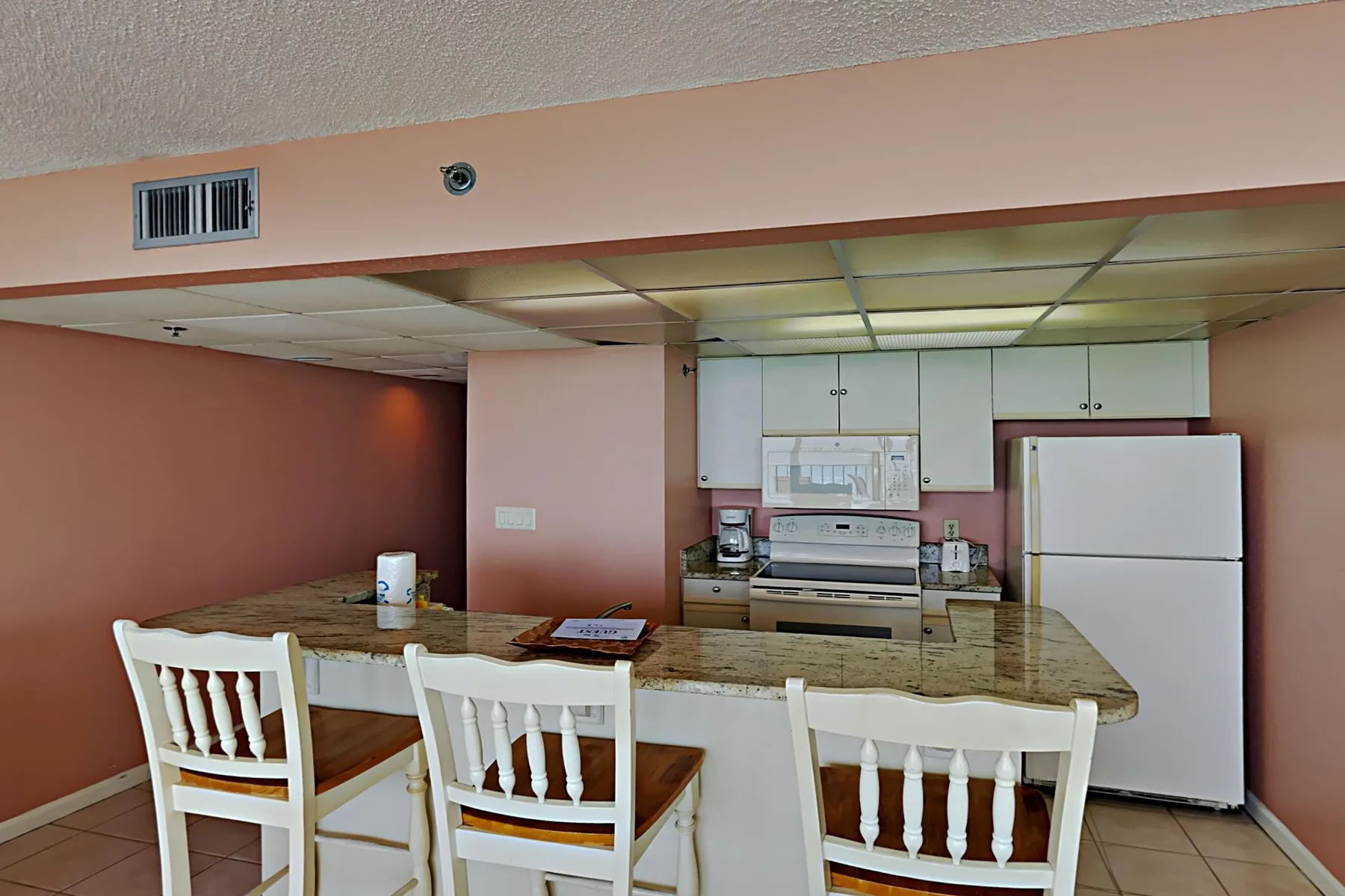 A kitchen with white cabinets, a refrigerator, and a breakfast counter with seating.