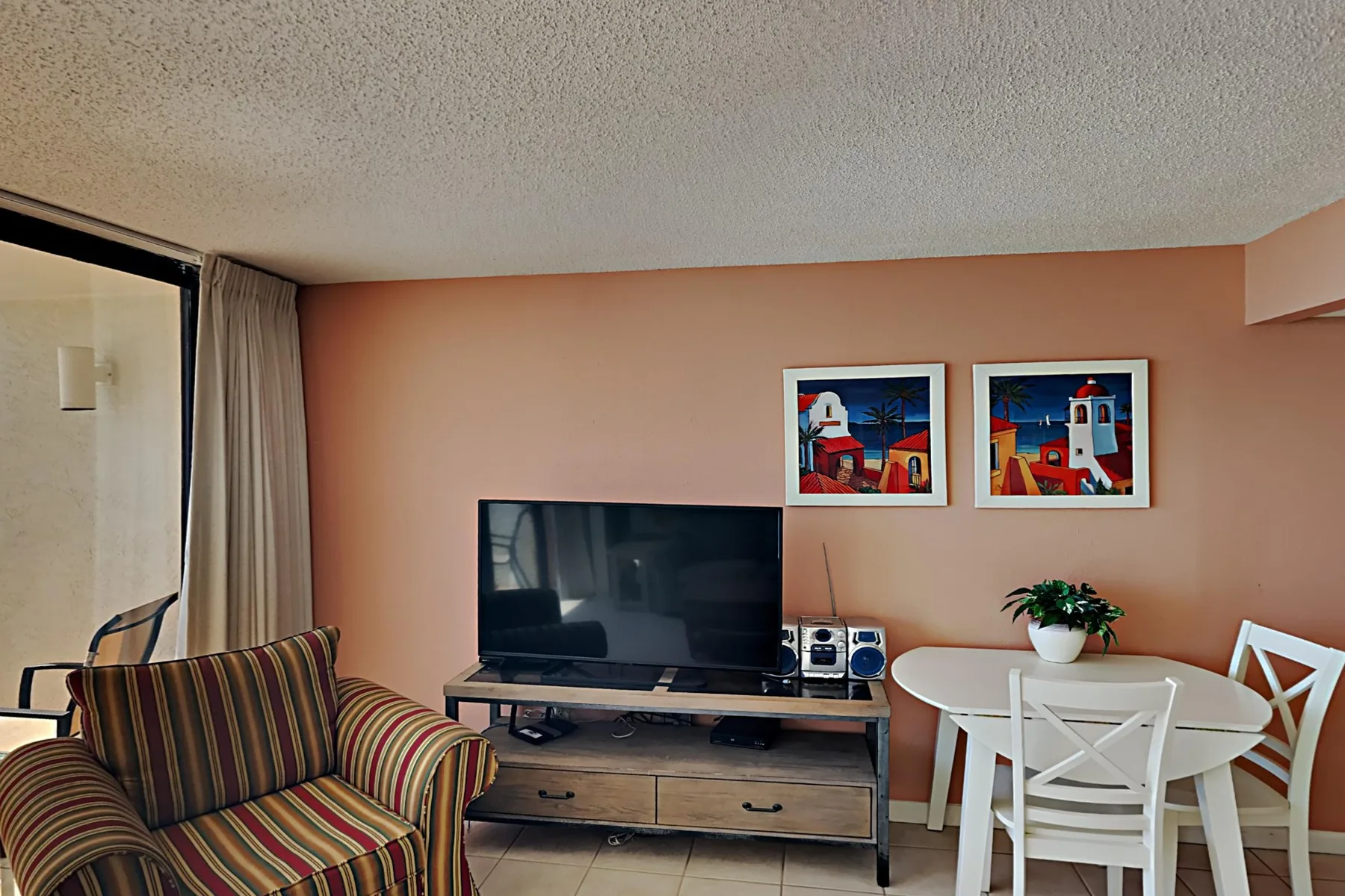 A living area with a television, striped seating, and a small dining table.