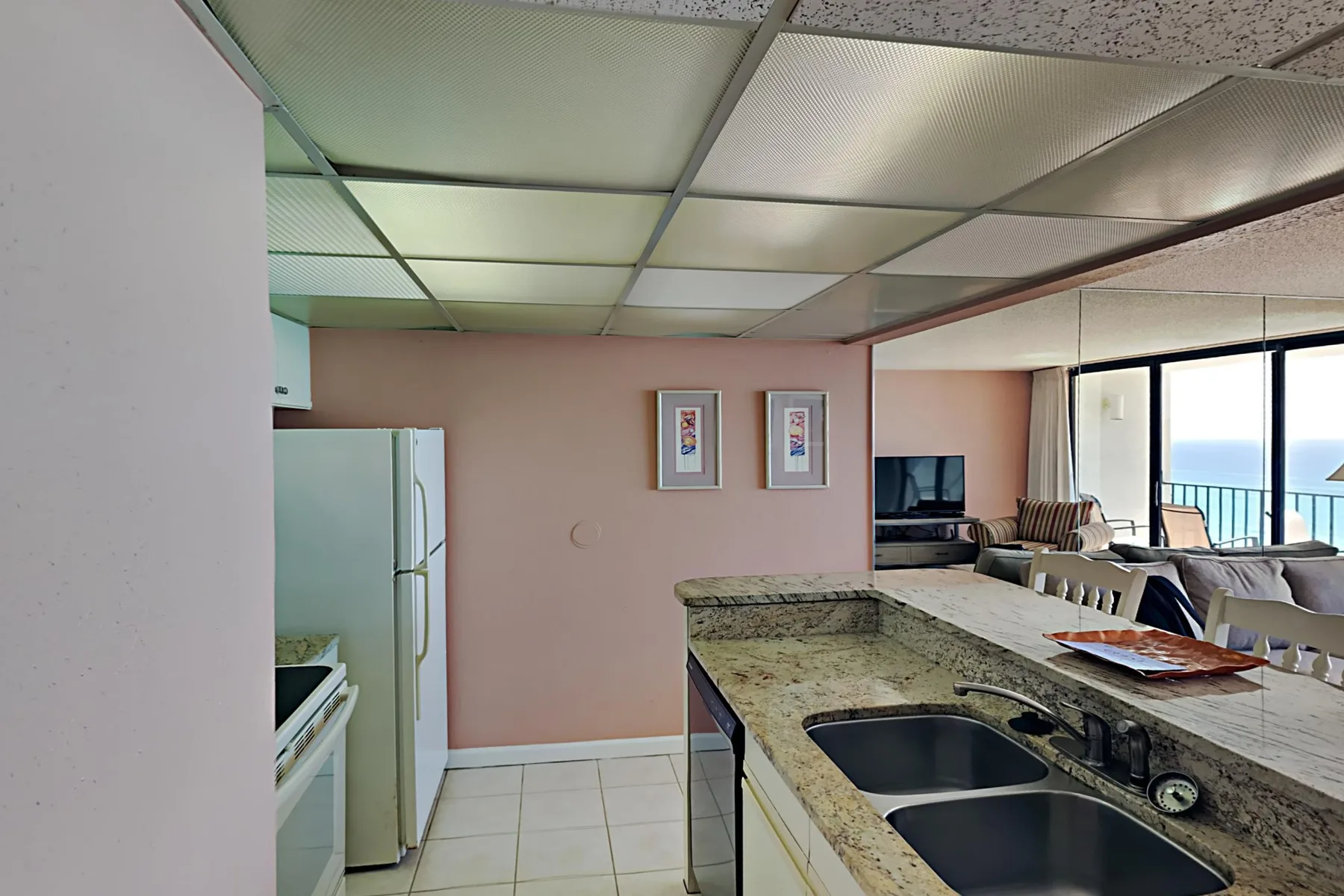 A kitchen with a long counter and sink opens into a living area.