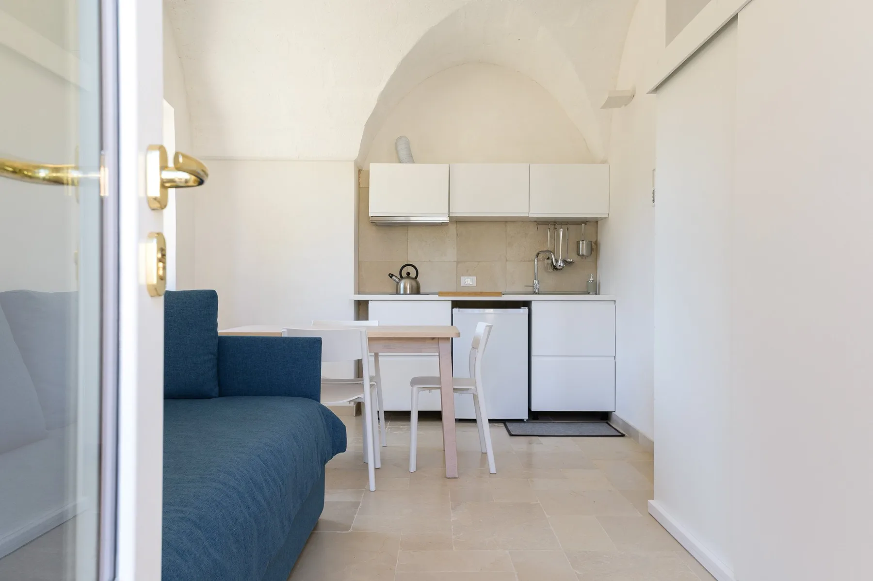 A compact kitchen and dining area with a blue sofa in the foreground.