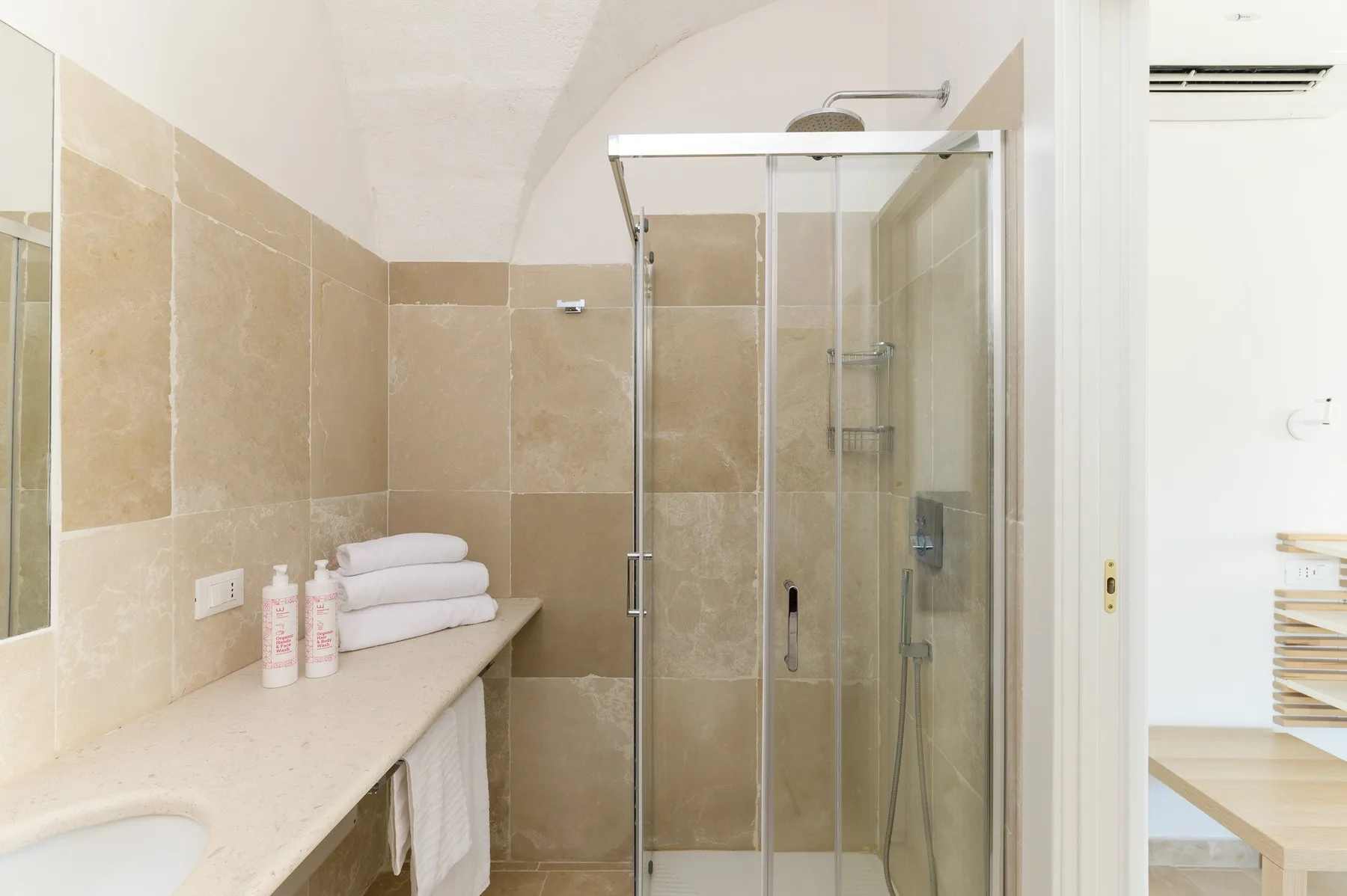 A tiled bathroom with a glass shower and folded white towels on the counter.