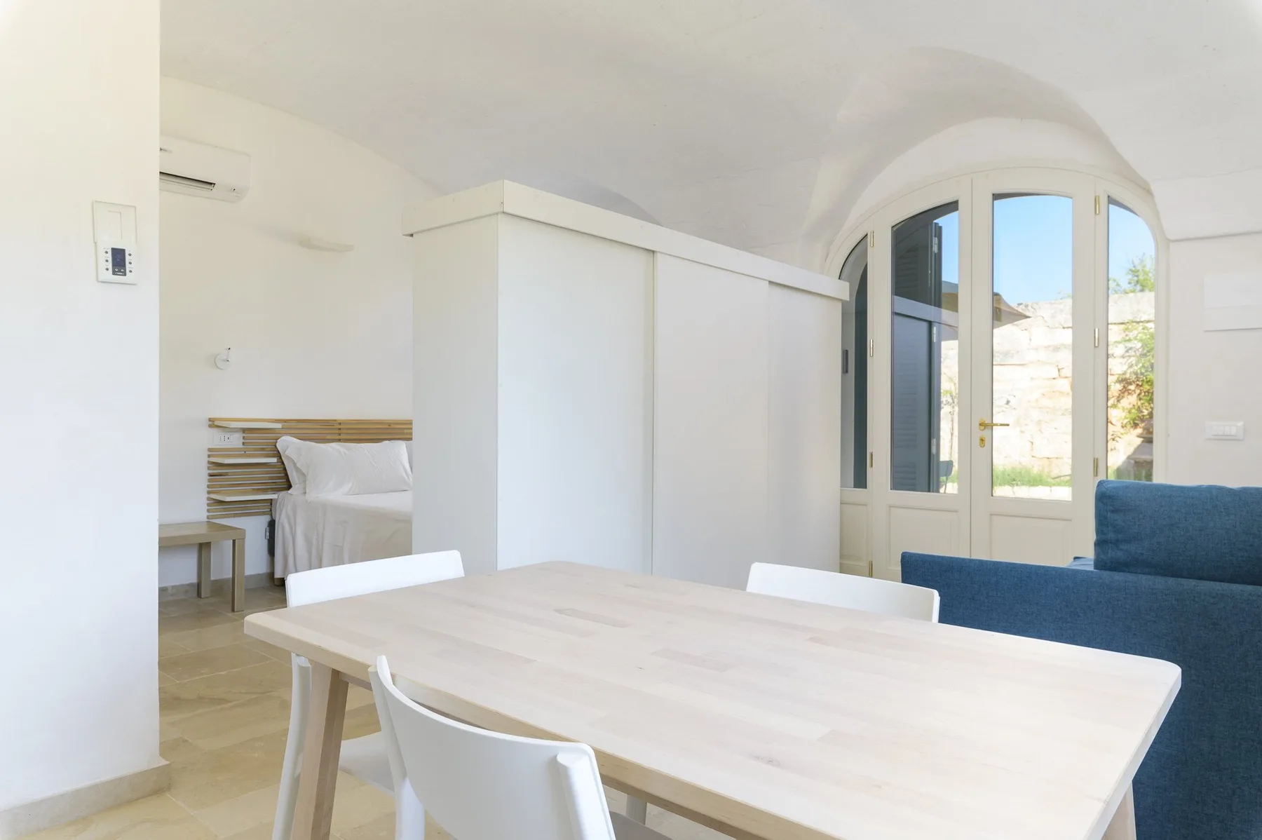 A bright dining area with a pale table and seating beside arched glass doors.