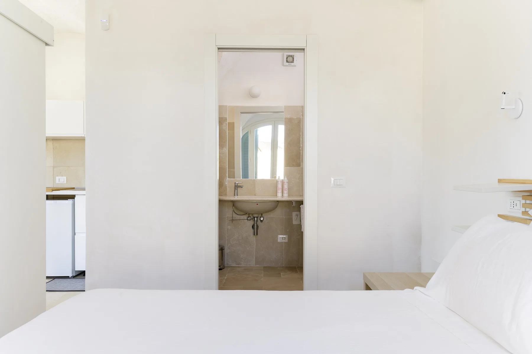 A bright bedroom with a bed facing an open doorway to a bathroom.