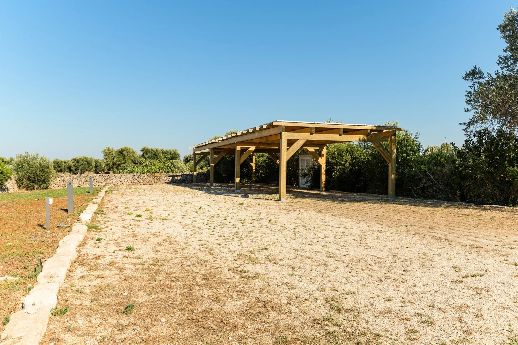 A covered wooden structure stands beside an open, dry field.