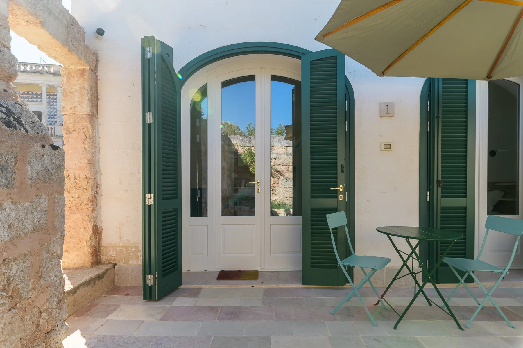 A patio with an arched glass doorway, green shutters, and outdoor seating.