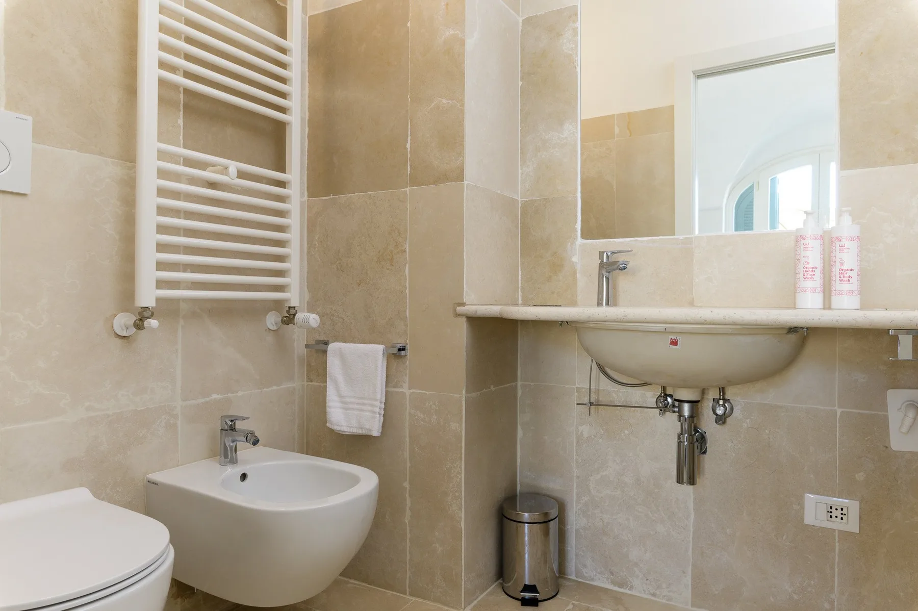 A tiled bathroom with a sink, toilet, and wall-mounted towel warmer.