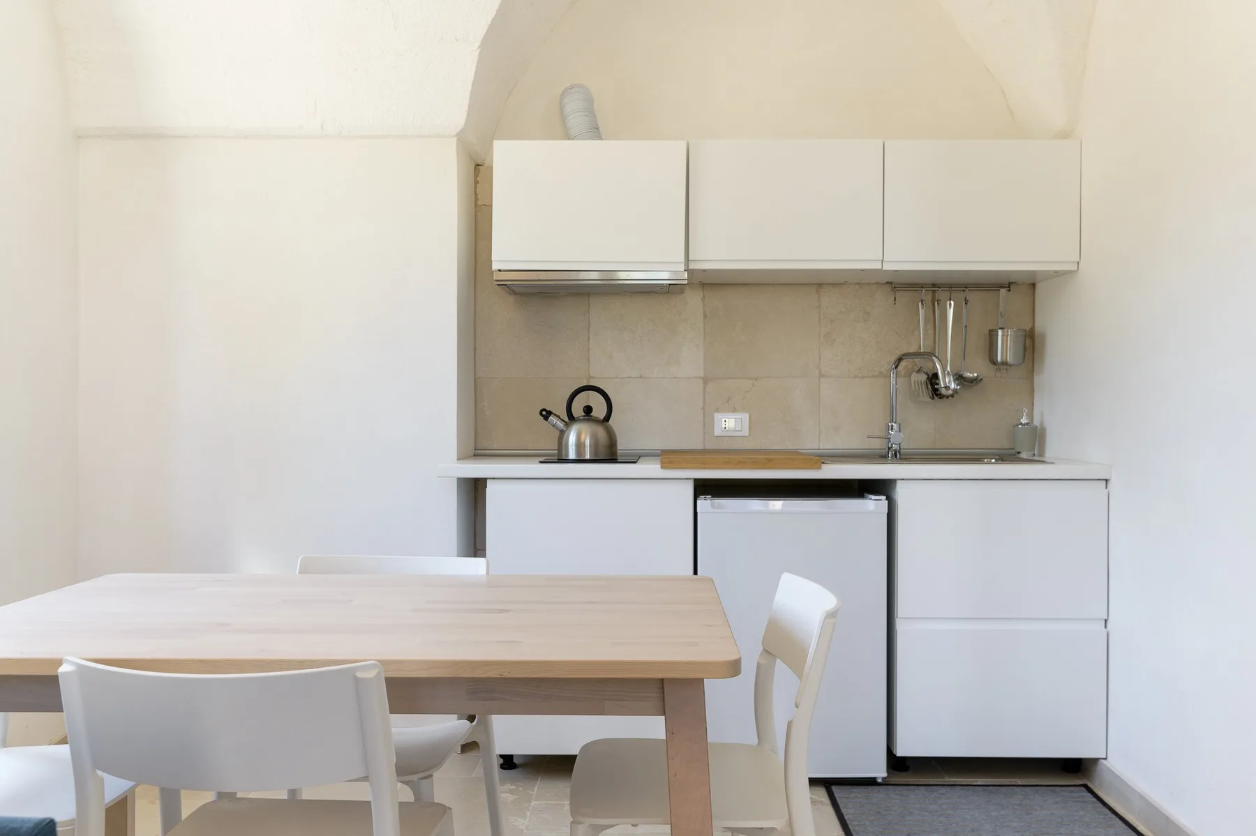 A compact kitchen with pale cabinets and a wooden dining table.