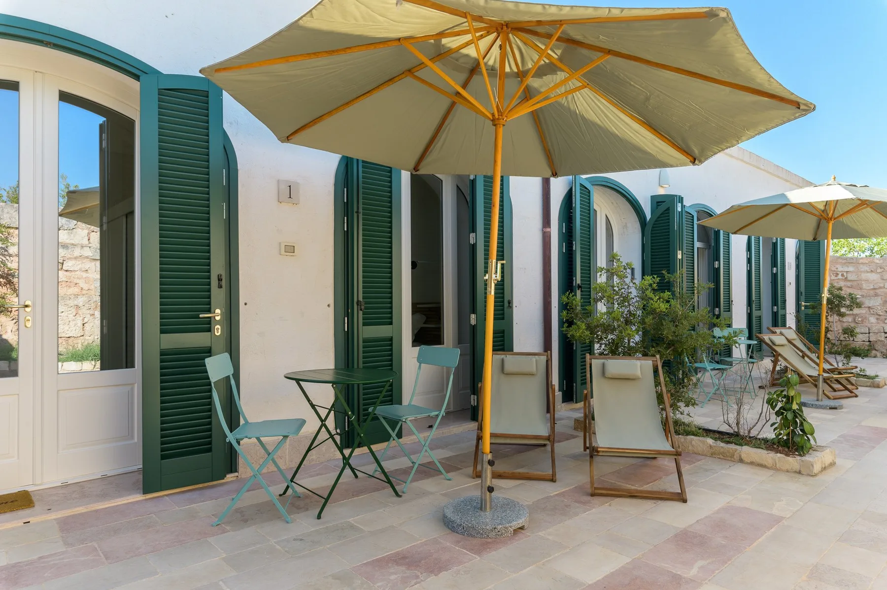 A shaded patio with outdoor seating and large umbrellas beside a white building.