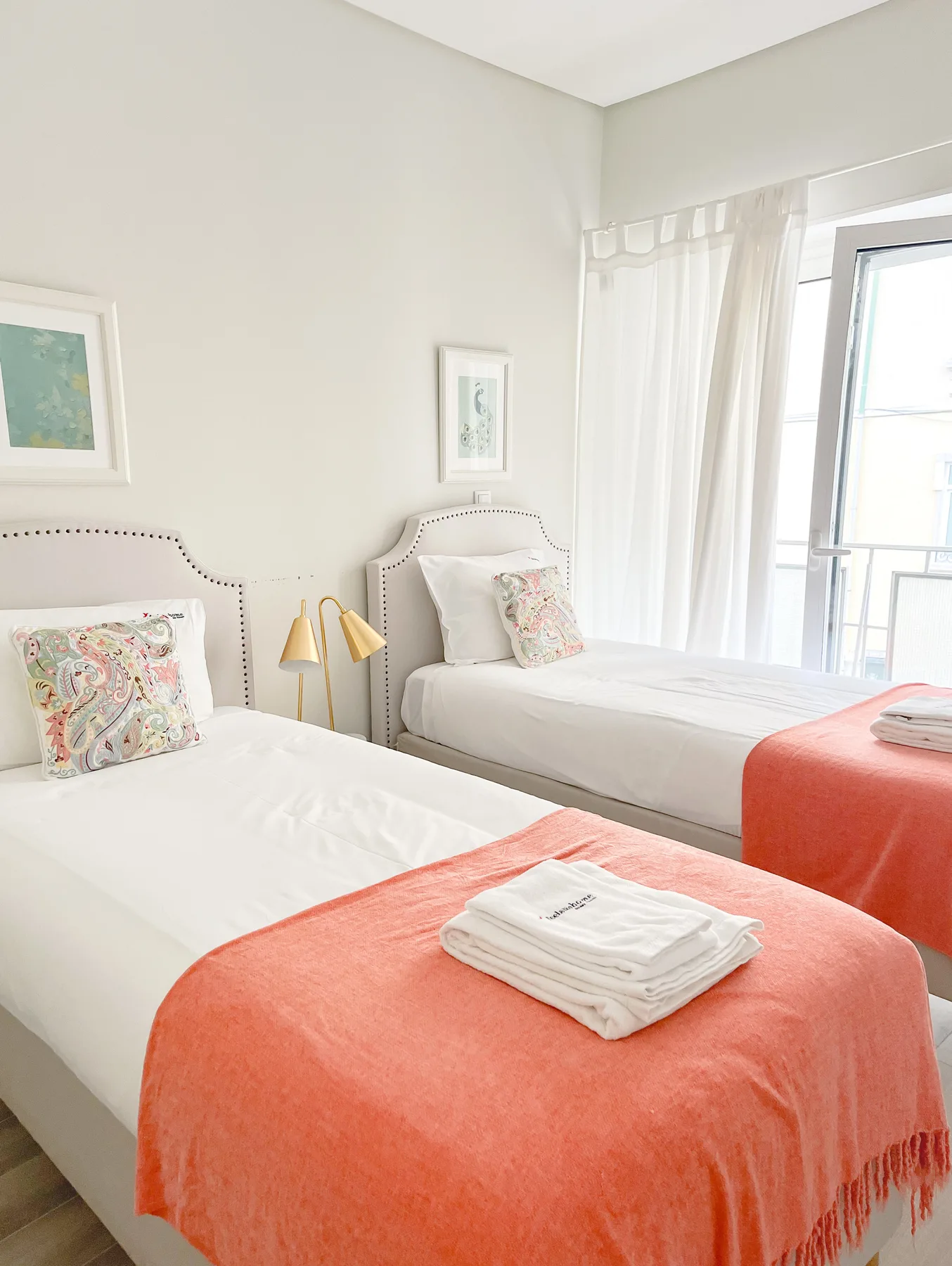 A bright bedroom with two beds dressed in white linens and coral throws.
