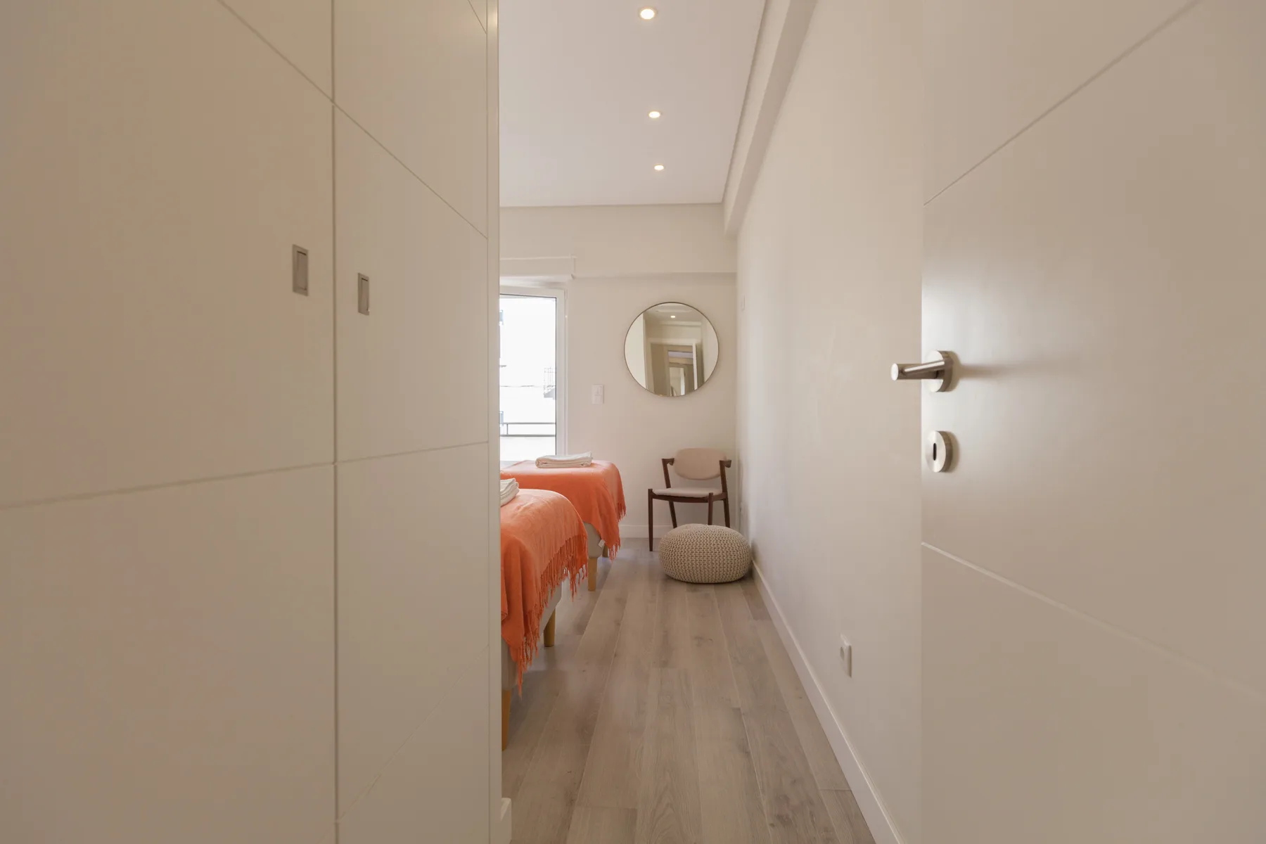 A bedroom with orange bedding and a chair beside a round mirror.