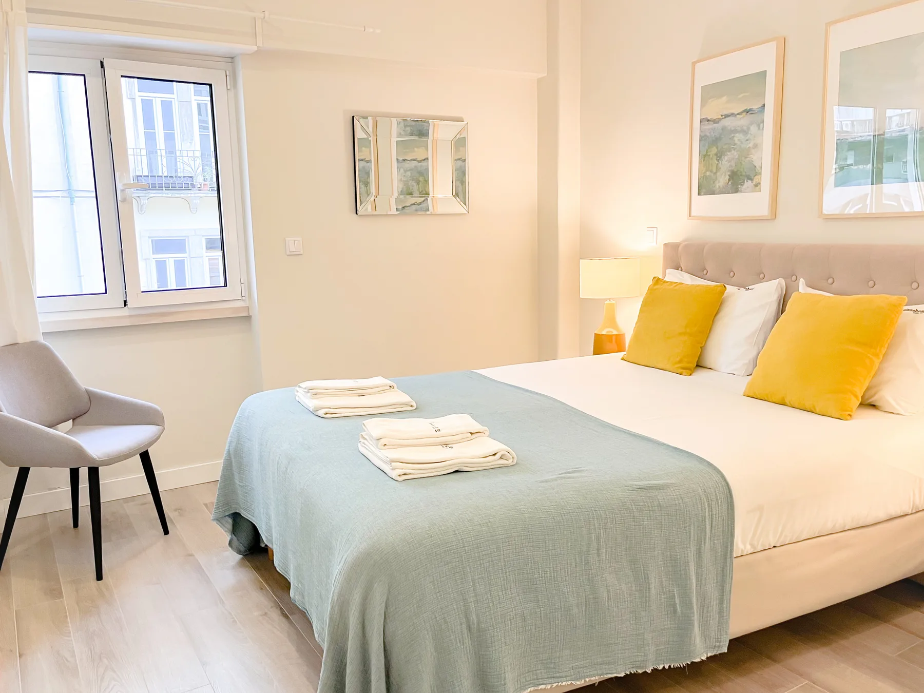 A bedroom with a neatly made bed, yellow pillows, and a window.