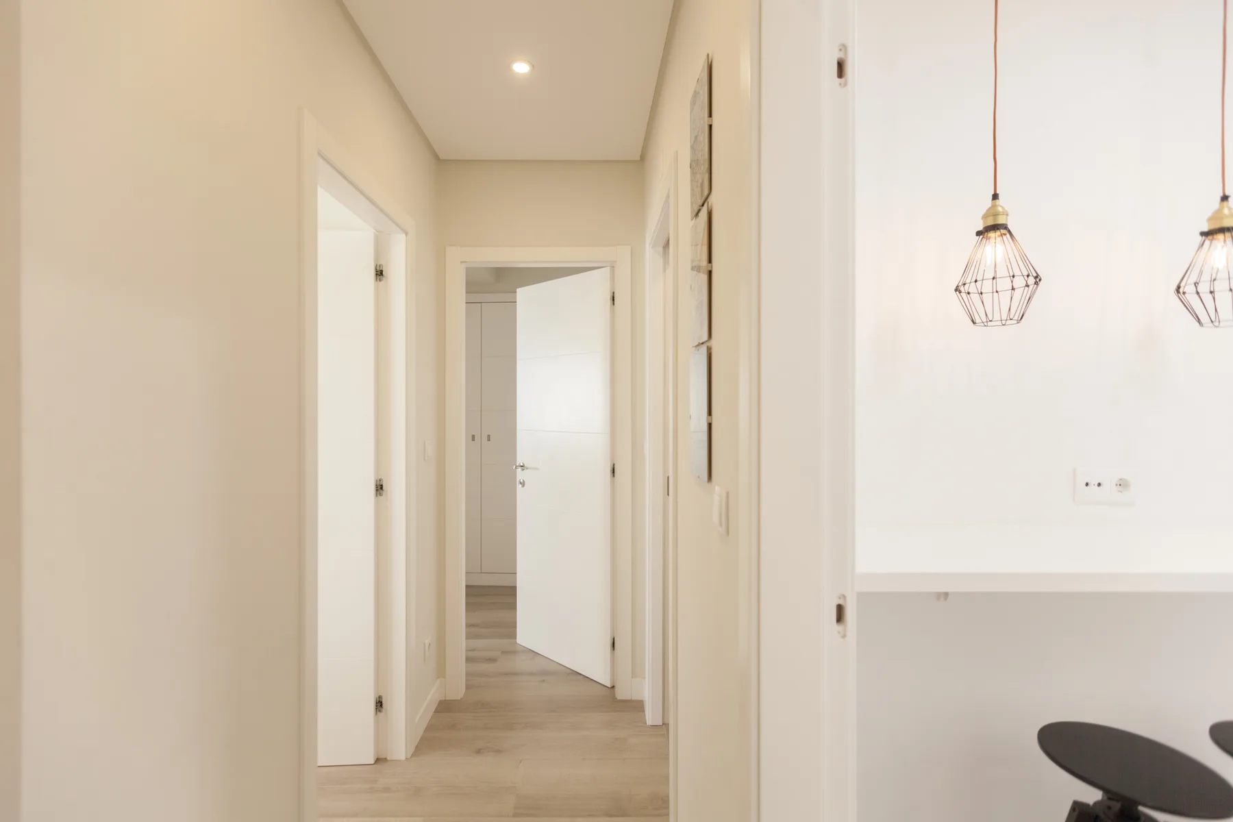 A bright hallway opens into a room with pendant lights and seating.